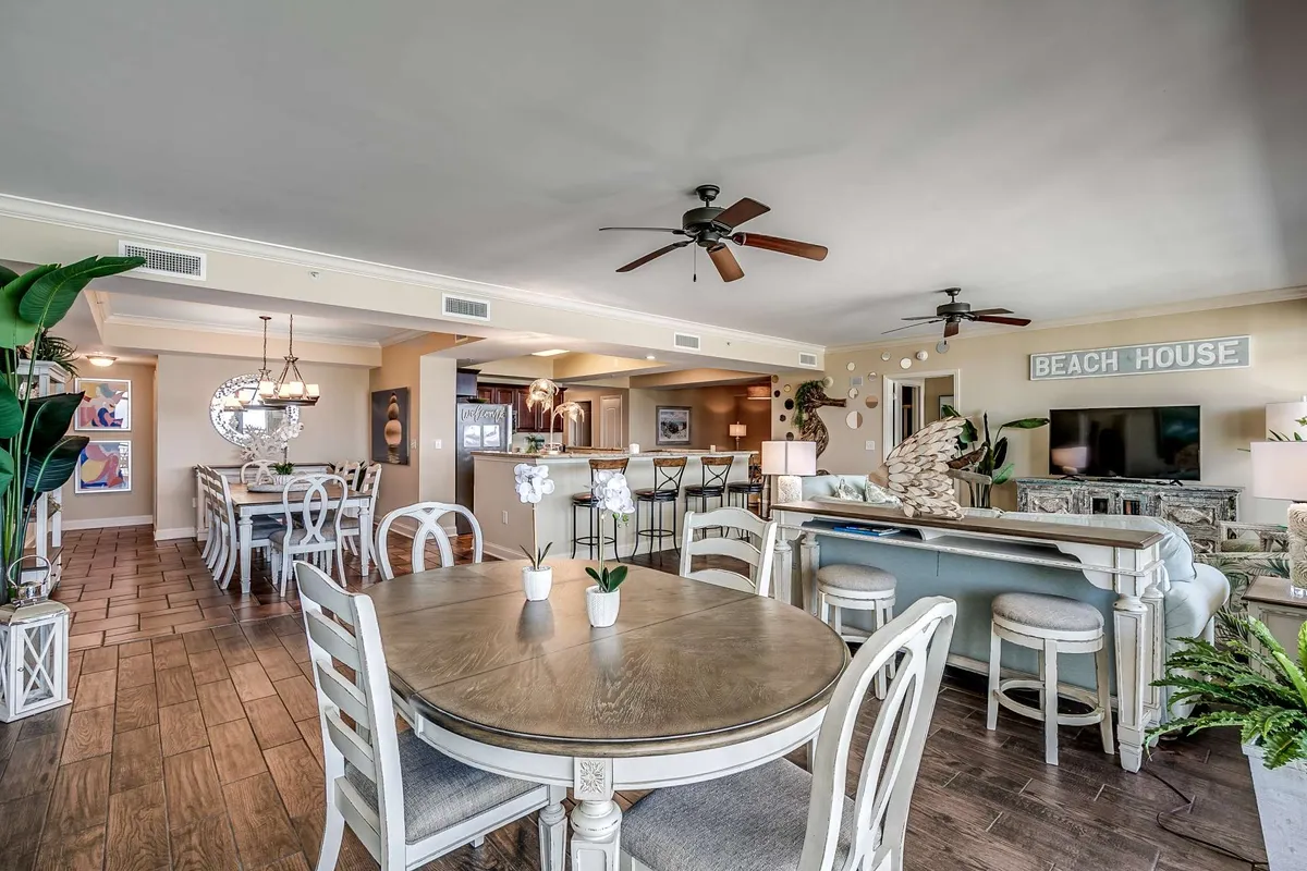 A wide-angle view of the dining area, highlighting a large table with a decorative plant, open kitchen layout, and spacious living area. The scene suggests space for large family meals, celebrations, and shared experiences.