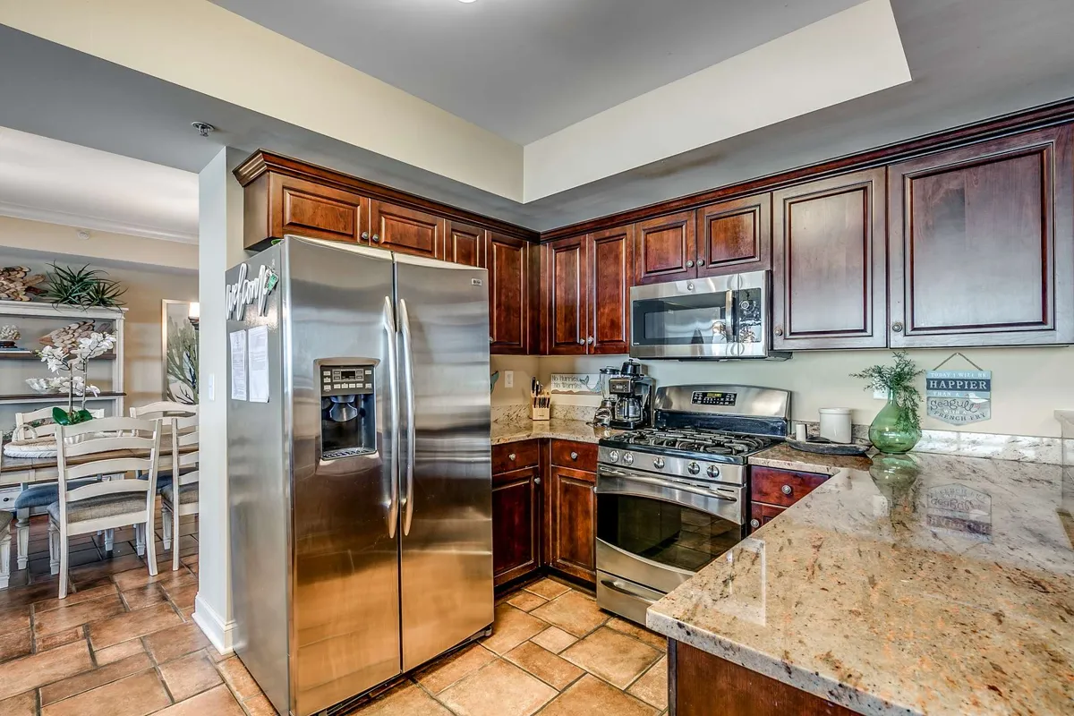 This image showcases a modern kitchen with a stainless steel refrigerator, granite countertops, and wood cabinetry, capturing the essential elements of a gourmet cooking environment. The inviting setup is perfect for both preparing meals and social gatherings.