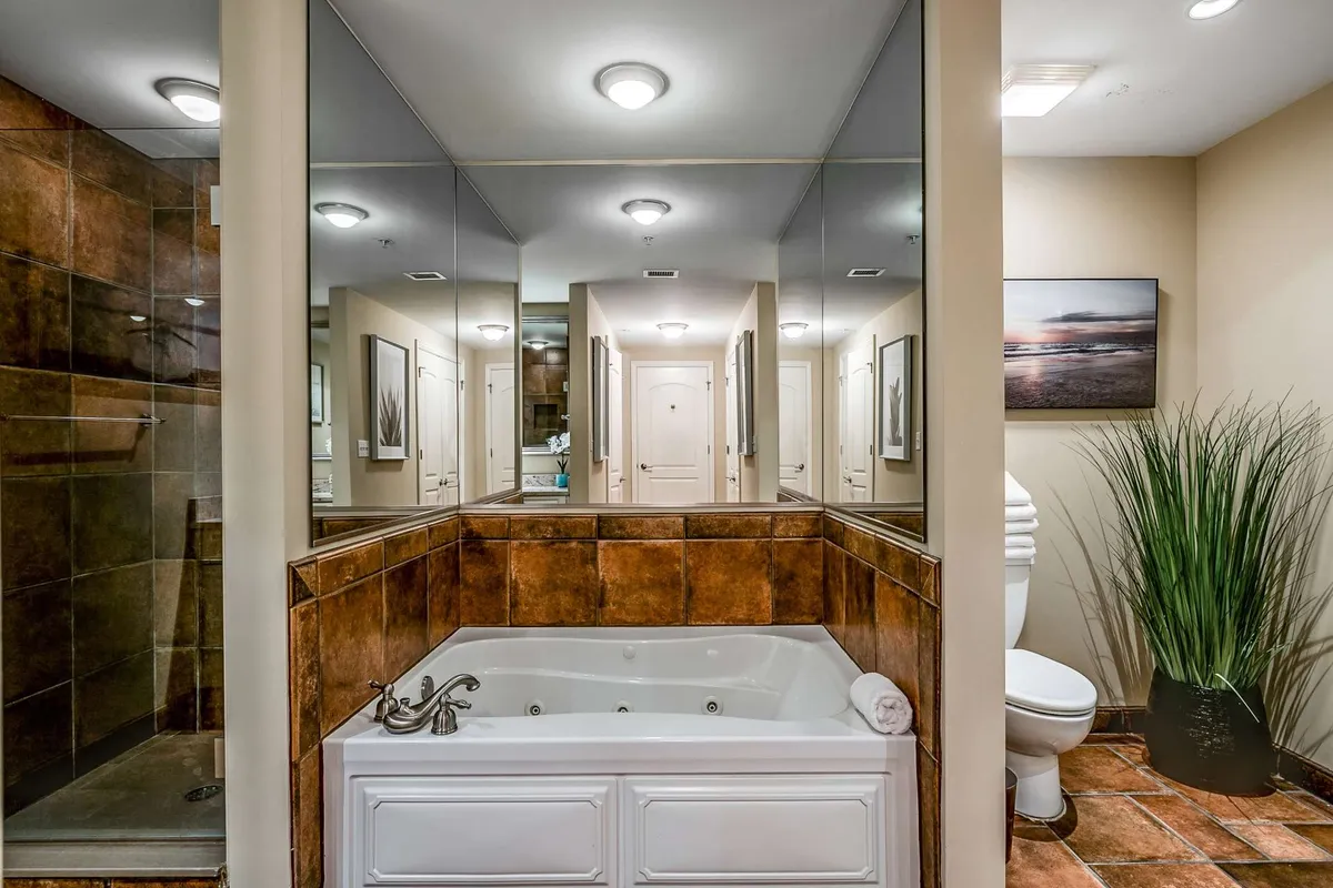 A luxurious bathroom with a jacuzzi tub, mirrored walls, a separate shower area, and decorative touches like a plant and framed artwork. The serene mood invites relaxation, perfect for a rejuvenating soak after a day of adventure.