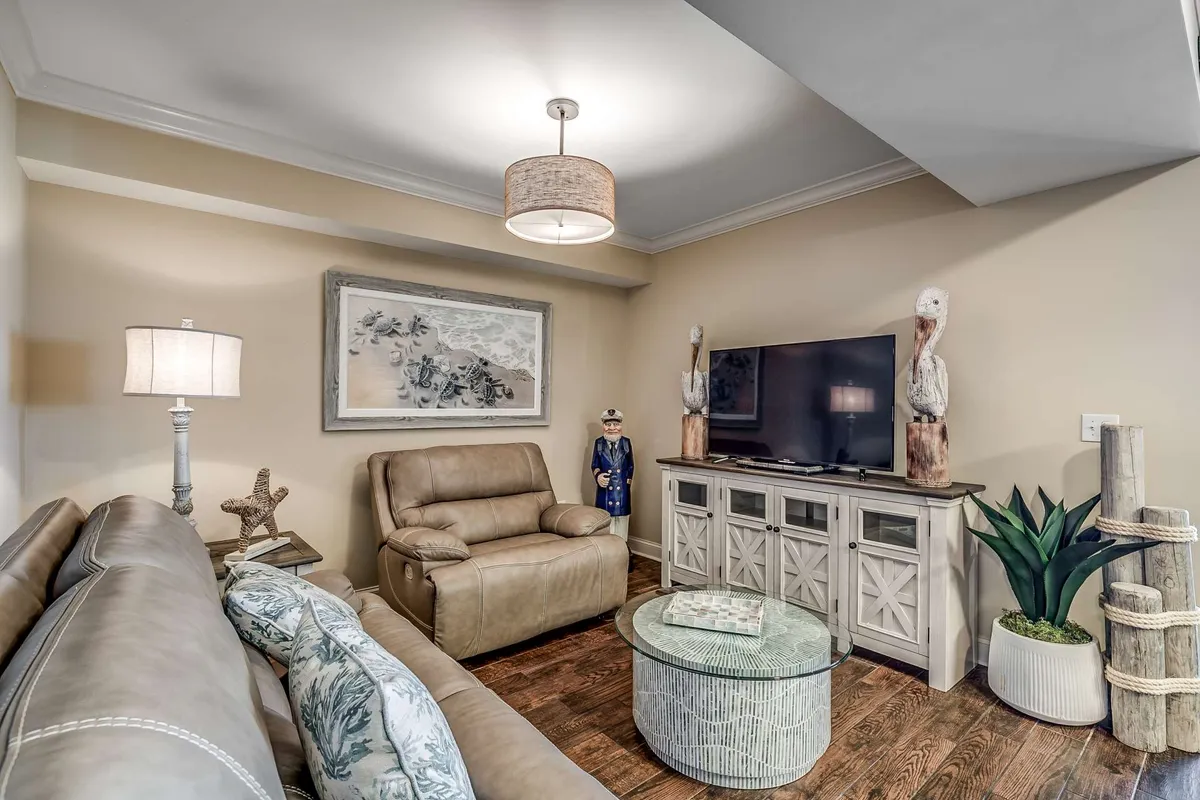A cozy interior shot highlighting a leather recliner, television set, decorative figurines, framed artwork, and a plant. The arrangement creates a welcoming atmosphere ideal for family movie marathons, quiet reading, or game nights with friends.