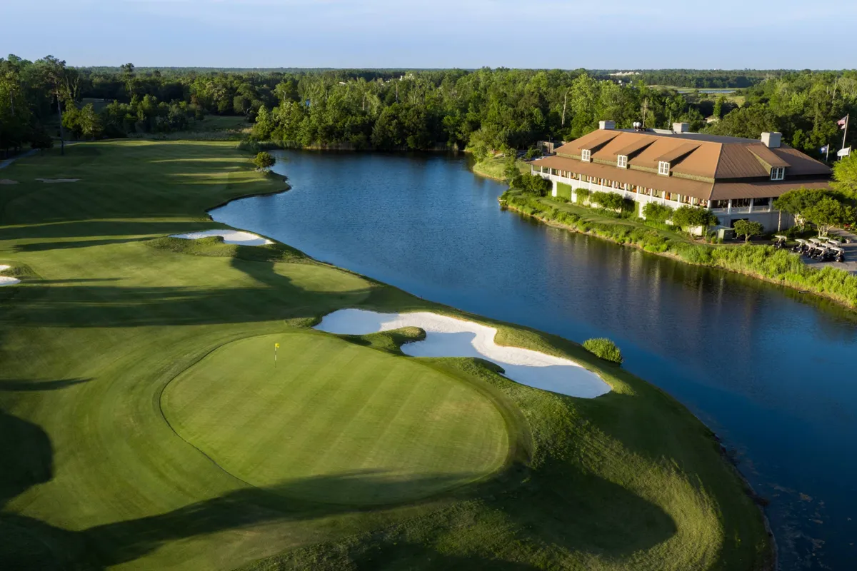 This image showcases a lush golf course featuring well-manicured greens, a clubhouse, a reflective water body, and sand traps set against a relaxed, natural backdrop. The environment is open and inviting, perfect for enjoying a round of golf or a leisurely walk.