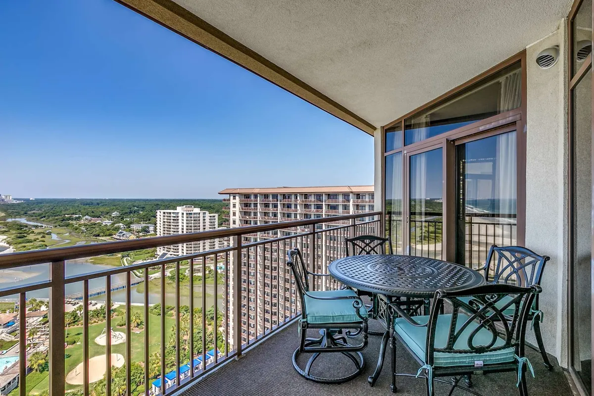 This image shows a spacious balcony with comfortable seating and a table setting, overlooking a scenic landscape. The outdoor space invites small groups to gather, enjoy meals, or relax together while taking in the view.