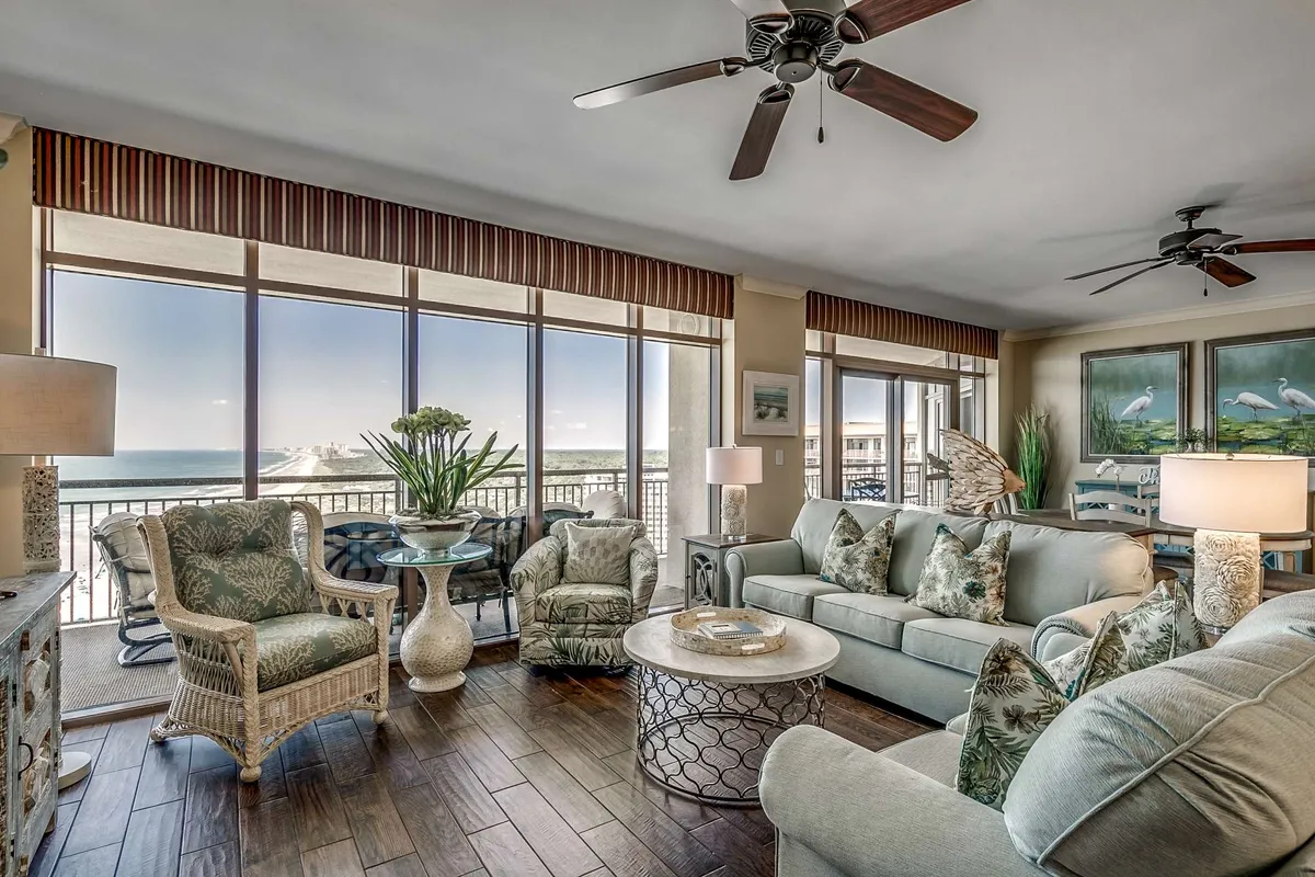 The image showcases a spacious, stylish living area with comfortable seating arranged to face floor-to-ceiling windows, offering breathtaking panoramic views of the Atlantic Ocean. Soft natural light fills the room, highlighting tasteful coastal décor, lush decorative plants, and elegant wall art. The serene setting invites guests to unwind, socialize, or simply soak in the tranquil ocean vistas.