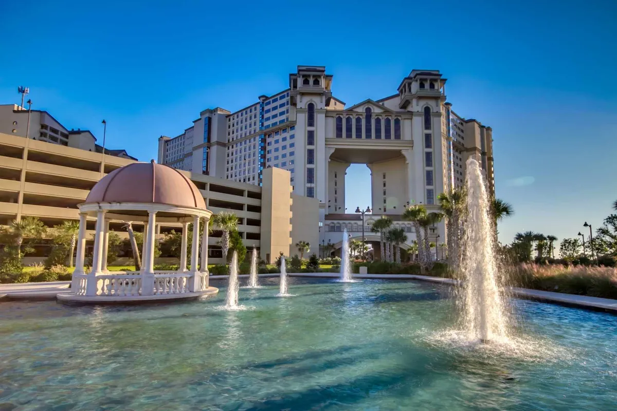 An elegant architectural structure featuring a water fountain, a classic gazebo, lush landscaping, and serene water views. The setting is refined and picturesque, evoking a high-end, resort-style environment ideal for relaxation or special gatherings.